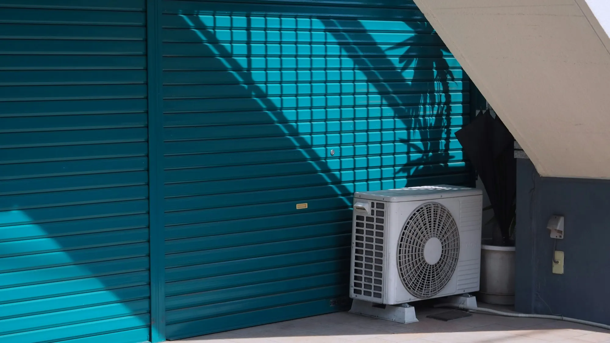 Outdoor AC condenser against a teal garage wall